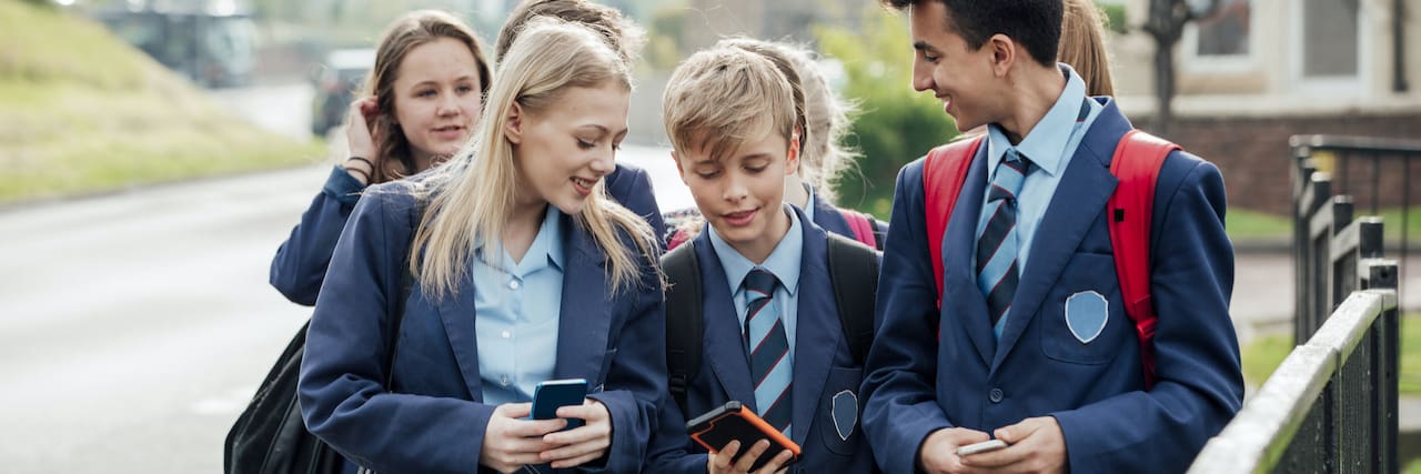 Group of teenage students walking home from school together on their phones