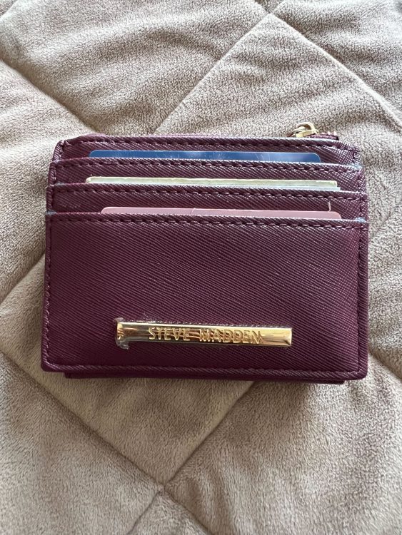 A purple wallet with some cards sticking out of it against a brown quilt