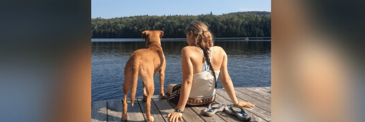 I Was Denied a Service Dog Because of My Mental Illness A golden yellow pit bull/vizsla mix and a girl with a ponytail sitting on the edge of a dock, looking out over a lake