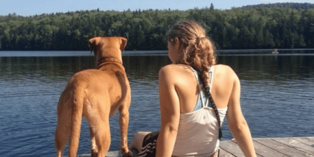 I Was Denied a Service Dog Because of My Mental Illness A golden yellow pit bull/vizsla mix and a girl with a ponytail sitting on the edge of a dock, looking out over a lake