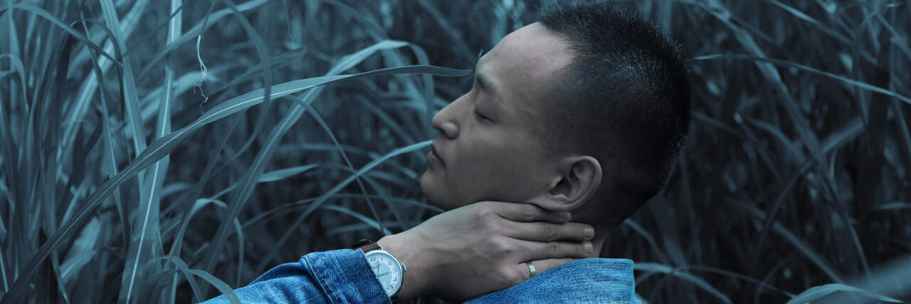 Man sitting in a field with eyes closed and hand on his neck, meditating
