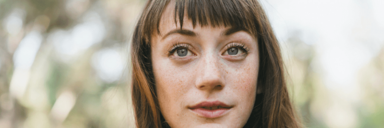 Taking Medication for Bipolar Mania Helped Give Me Confidence to Start a Family Woman looking ahead with neutral expression, with trees blurred in the background