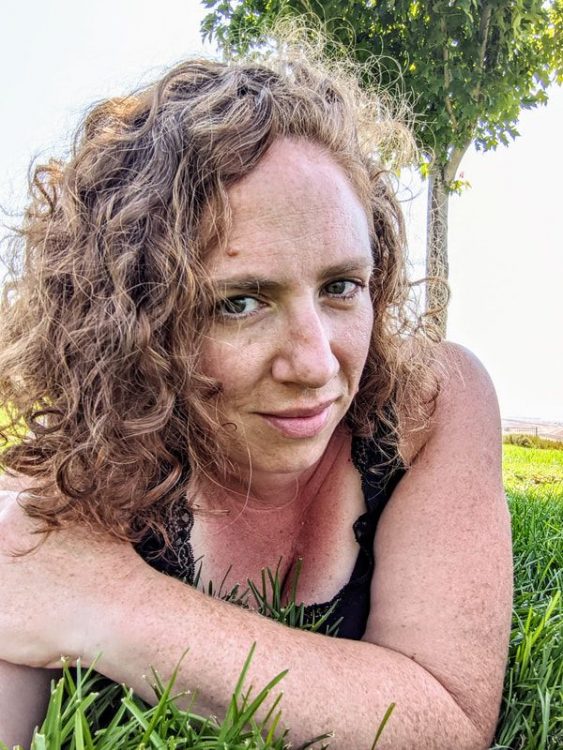 The author, a woman with curly brown hair, lies on her stomach on the grass.