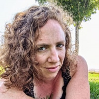The author, a woman with curly brown hair, lies on her stomach on the grass.