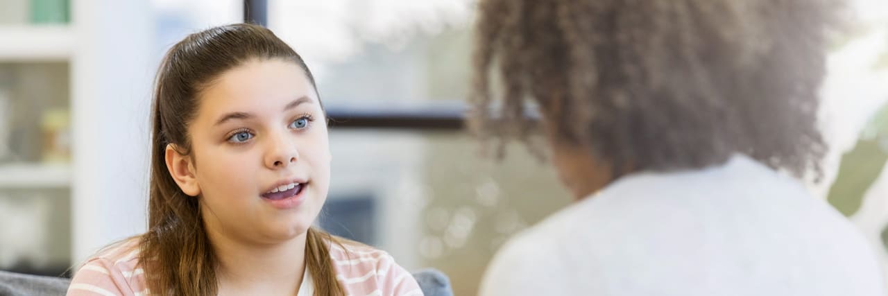 Finding My Voice and Advocating as a Teen With Complex Regional Pain Syndrome A teenage girl with brown hair and blue eyes wearing a striped shirt talks with a doctor.