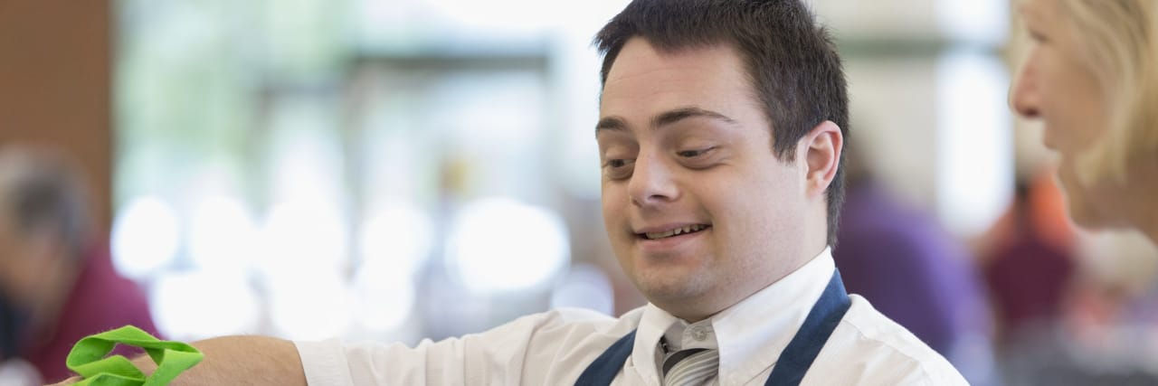 A man with down syndrome wearing an apron fills a reusable grocery bag.