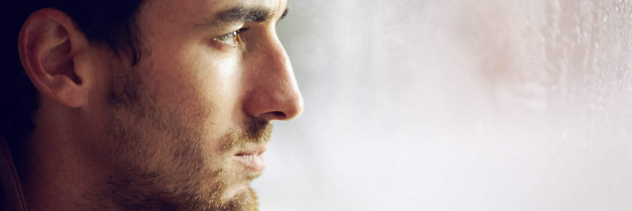 Finding a Treatment Plan After Years With Functional Neurological Disorder A man with brown hair and brown eyes looks out a window with his hands under his chin.