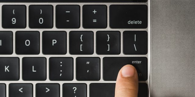 Overhead view of cropped finger pressing enter key on laptop computer's keyboard