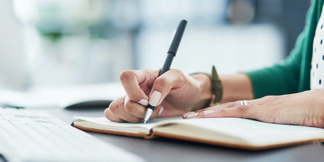 Hand holding pen on paper in journal at desk