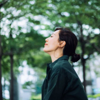 Asian woman standing outside in front of trees with her eyes closed, looking peaceful