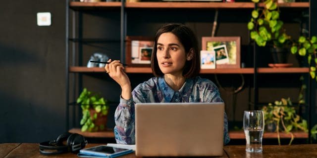 Woman holding a pen and sitting in front of a laptop