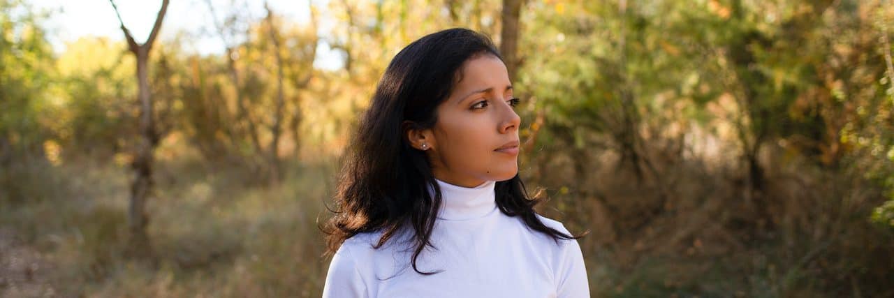 Why Breast Cancer Awareness Month Is so Hard Woman standing in front of autumn leaves on trees and looking to the side
