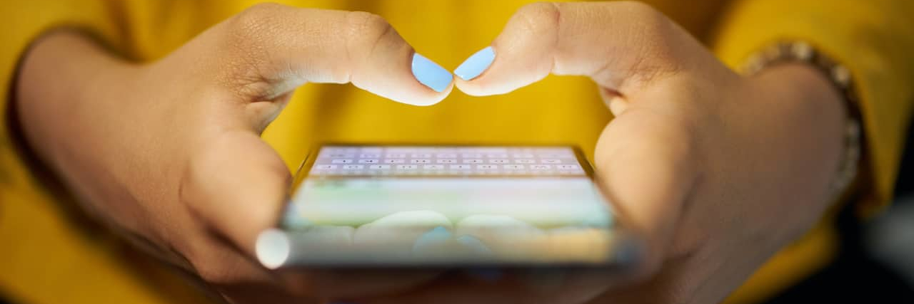 Close up of person's hands with light blue nail polish typing on a phone