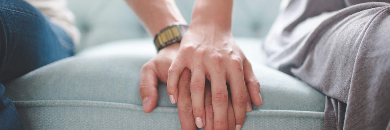 Close up of two people holding hands while sitting on a couch