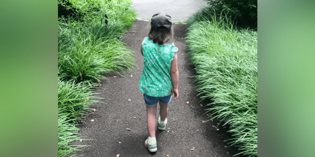 Photo of young girl from behind, walking on path surrounded by greenery