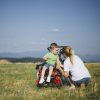 Mother crouching by young son in wheelchair in field