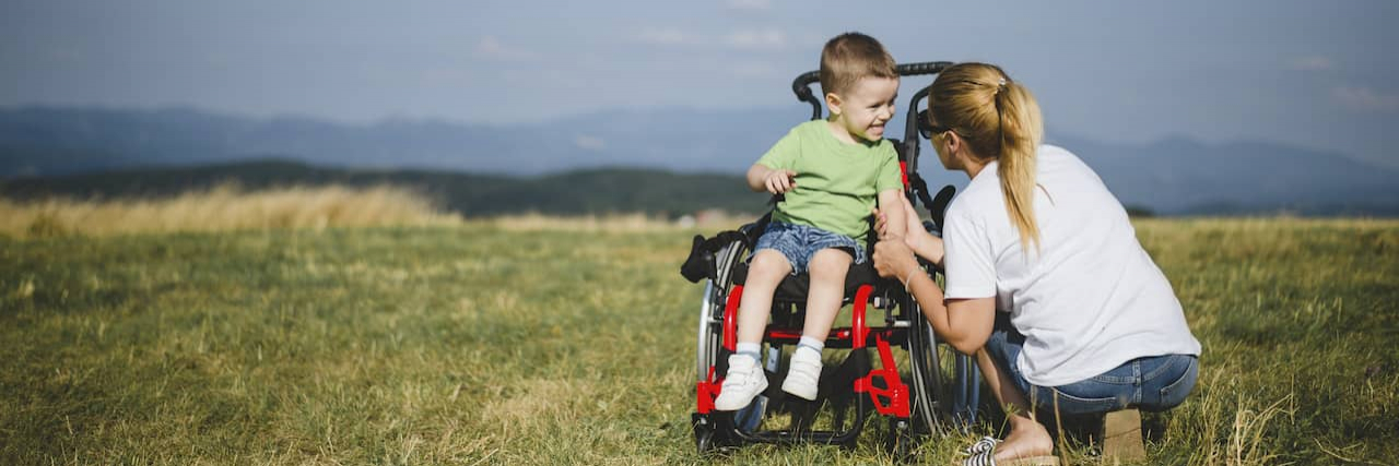 Mother crouching by young son in wheelchair in field