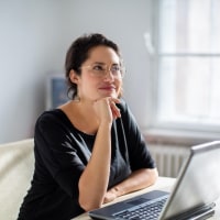 Woman sitting next to laptop and looking away as if in thought