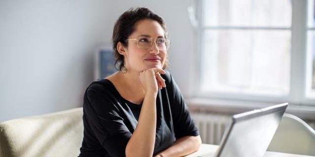 Woman sitting next to laptop and looking away as if in thought