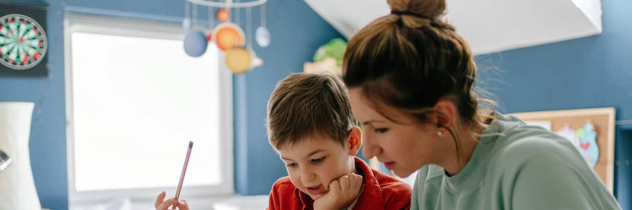 Mother and son in child's bedroom looking at workbook and holding a pencil