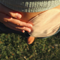 Close up of woman's stomach with an ostomy bag, standing outside on grass
