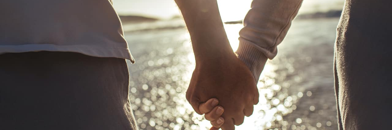 Helping the Well-Spouses and Family Caregivers in Your Life Cropped shot of couple holding hands on beach with sparkling water in front of them
