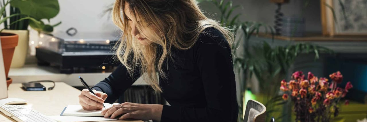 Thank You, Ulcerative Colitis, For Showing Me Who I Am blond woman making a to do list while sitting behind a desk in her living room