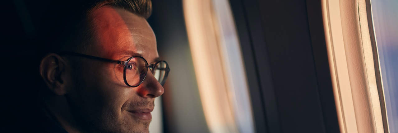 How Travel Helps My Social Anxiety and Special Interests as an Autistic Person Man looking through plane window with sun on his face