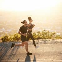 Two fit young friends in sportswear jogging together along a scenic road overlooking the city on a sunny afternoon
