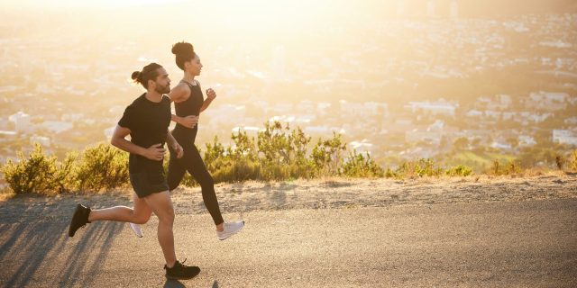 Two fit young friends in sportswear jogging together along a scenic road overlooking the city on a sunny afternoon