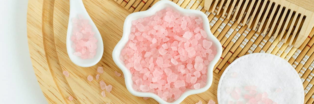 What I Keep in My Bathroom That Helps With Chronic Pain and Illness Small porcelain bowl and scoop with pink bath salts on a wooden tray