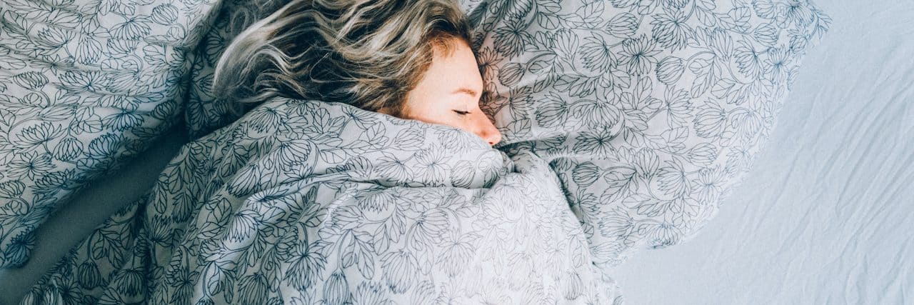 High Angle View Vie Of Woman Sleeping On Bed with covers pulled up to her face