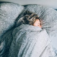 High Angle View Vie Of Woman Sleeping On Bed with covers pulled up to her face