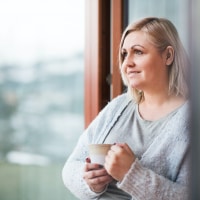 Woman at home slightly smiling, holding a mug