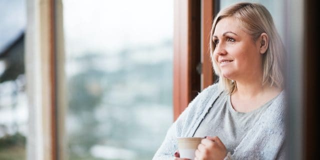 Woman at home slightly smiling, holding a mug