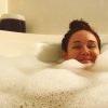Woman smiling in bath with head peeking out, surrounded by bubbles