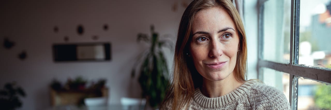 A New Year's Resolution to Choose Me and My Mental Health Woman at home smiling slightly next to window