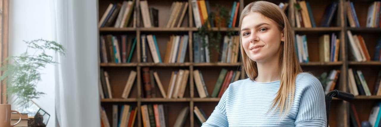 Young woman sitting in wheelchair with a slight smile, in front of bookshelves