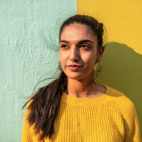 Portrait of Indian woman looking away while leaning on light blue/ yellow wall