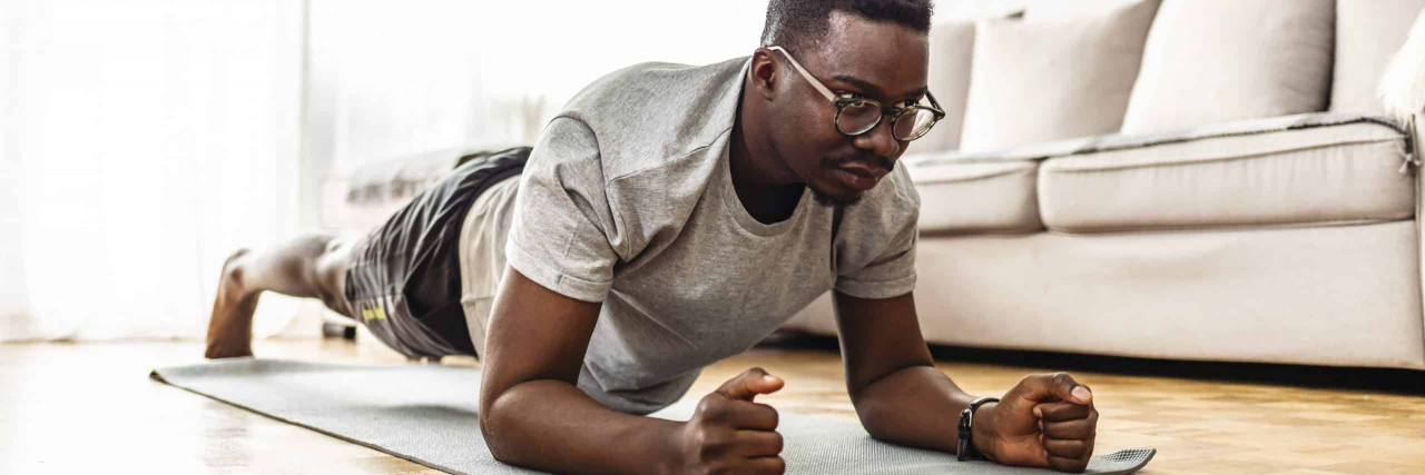 Self-Care Techniques That Ease My Bipolar Disorder Symptoms Confident muscled young man wearing sport wear and doing plank position while exercising on the floor in home interior.