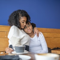 Black mother and daughter embracing in a cafe