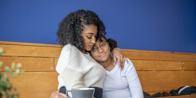 Black mother and daughter embracing in a cafe