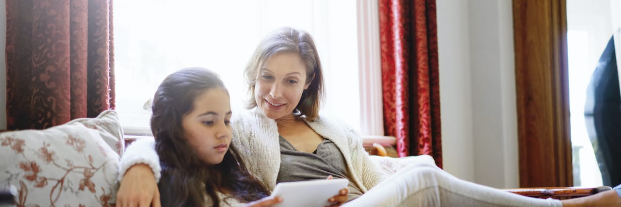 You teen using tablet while resting with mother.