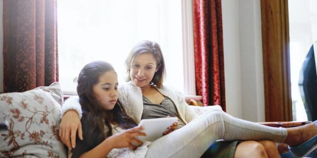You teen using tablet while resting with mother.