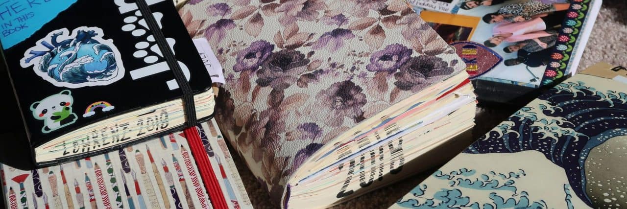 How Art Changed My Life With Chronic Pain and Mental Illness Journals and sketchbooks stacked on each other in a messy pile