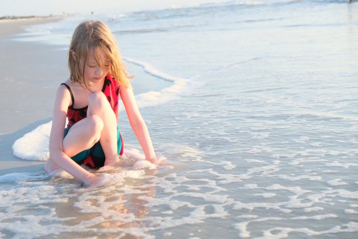 Blonde-haired child sits in shallow water at beach