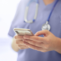 Close up of a medical professional's hands holding a phone, wearing scrubs and a stethoscope