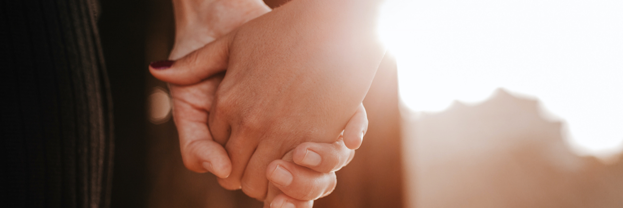 Close up on hands held together with sun streaming behind them