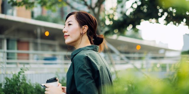 Asian woman outside with coffee in an urban park area