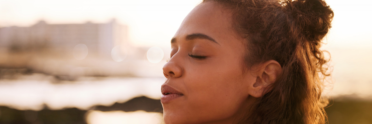 Woman of color with eyes closed looking peaceful outside at sunset
